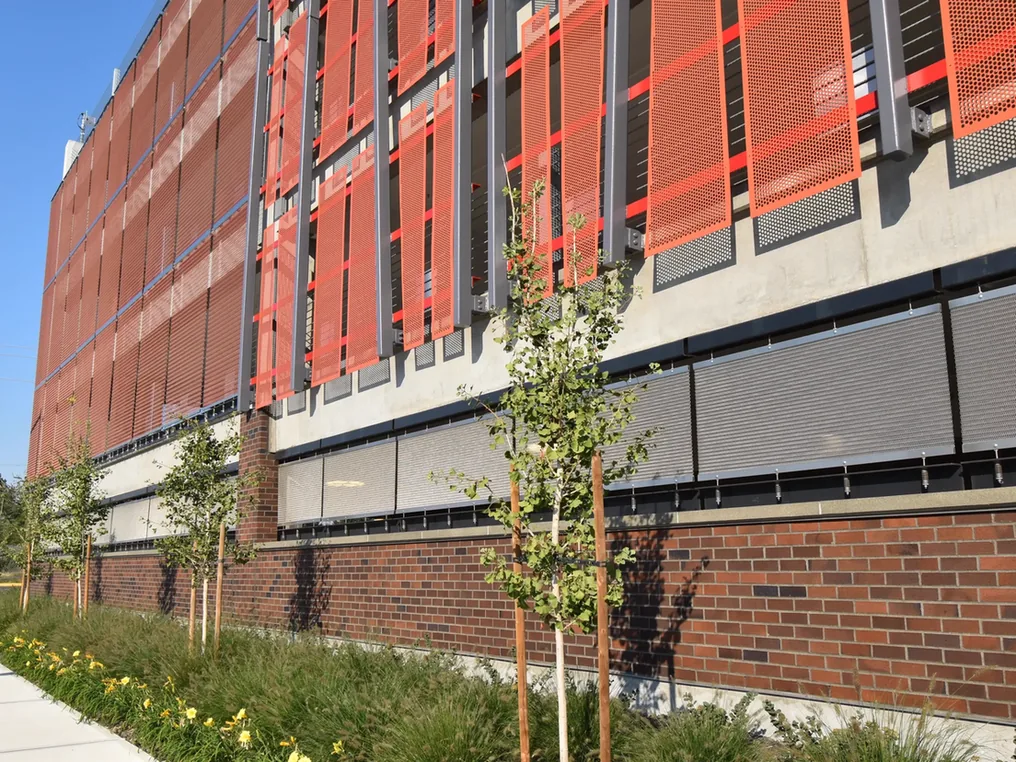 New brick wall along the base of a parking garage beside a planted sidewalk, brick masonry