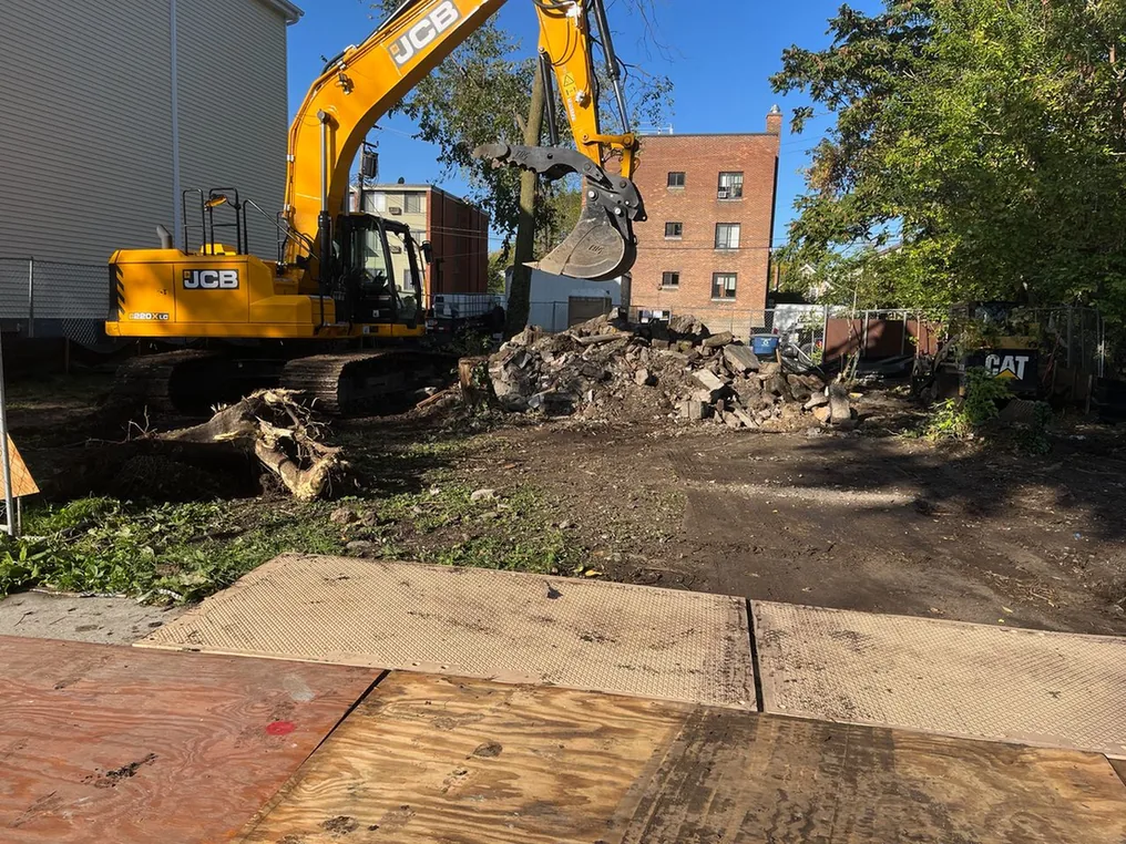 Excavator beside a rubble pile on a cleared lot next to a brick apartment building, building demolition