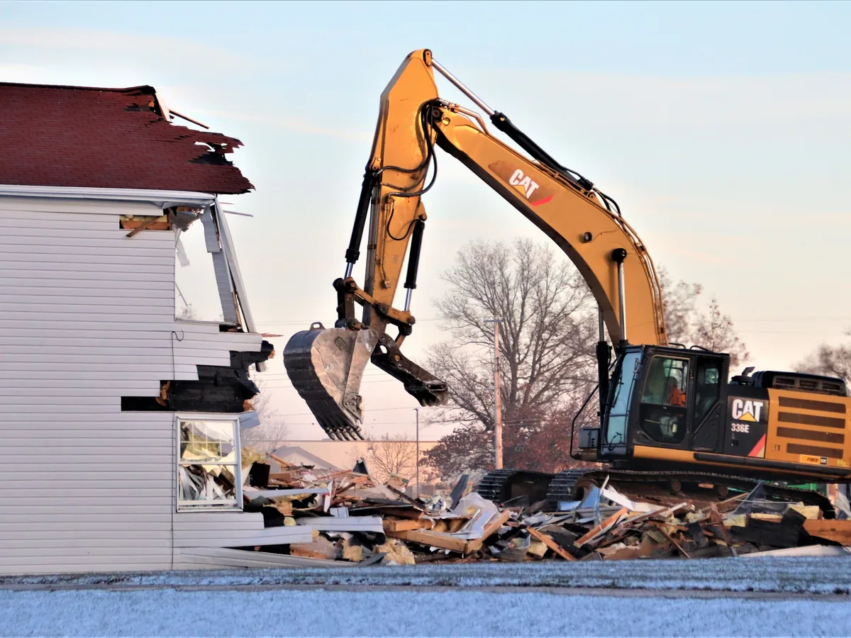 Excavator tearing apart a two story building with debris piled at its base, building demolition