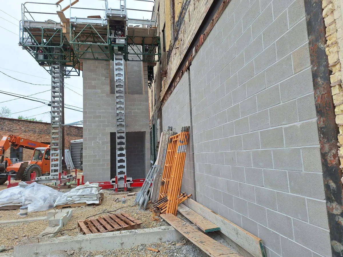 Concrete block shaft wall going up beside a mast climbing work platform, commercial masonry