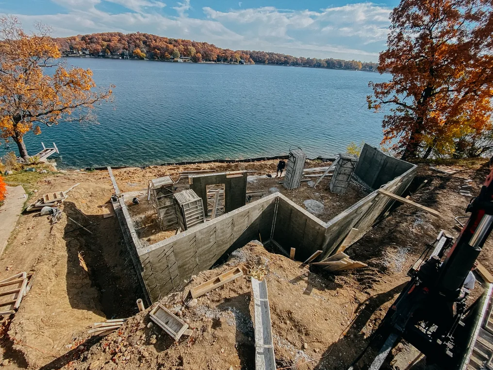 Freshly stripped poured concrete foundation walls for a lakeside house with autumn trees, concrete contractor