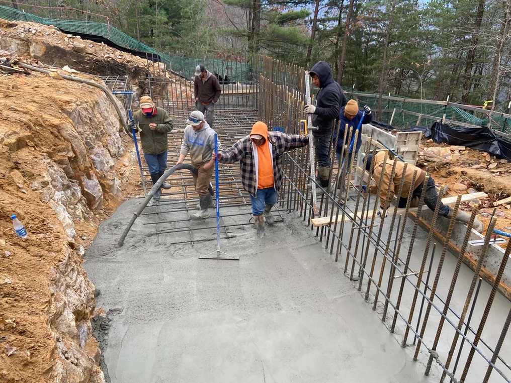Crew placing and screeding a reinforced concrete slab between rebar walls, concrete contractor