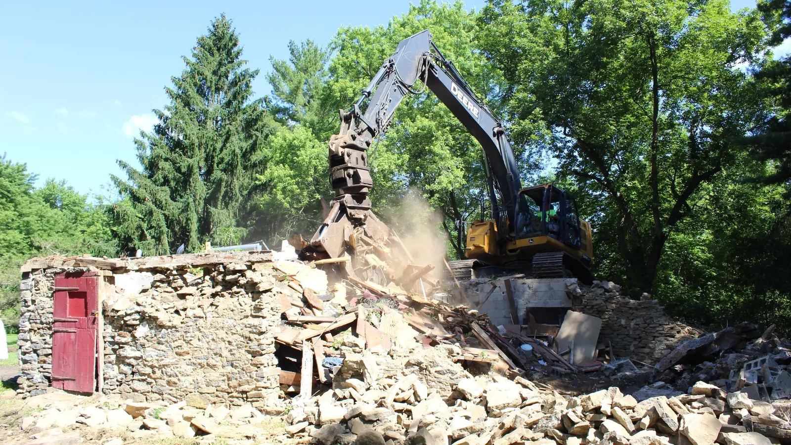 Excavator with a grapple knocking down an old fieldstone building into a pile of rubble, demolition and masonry contractor