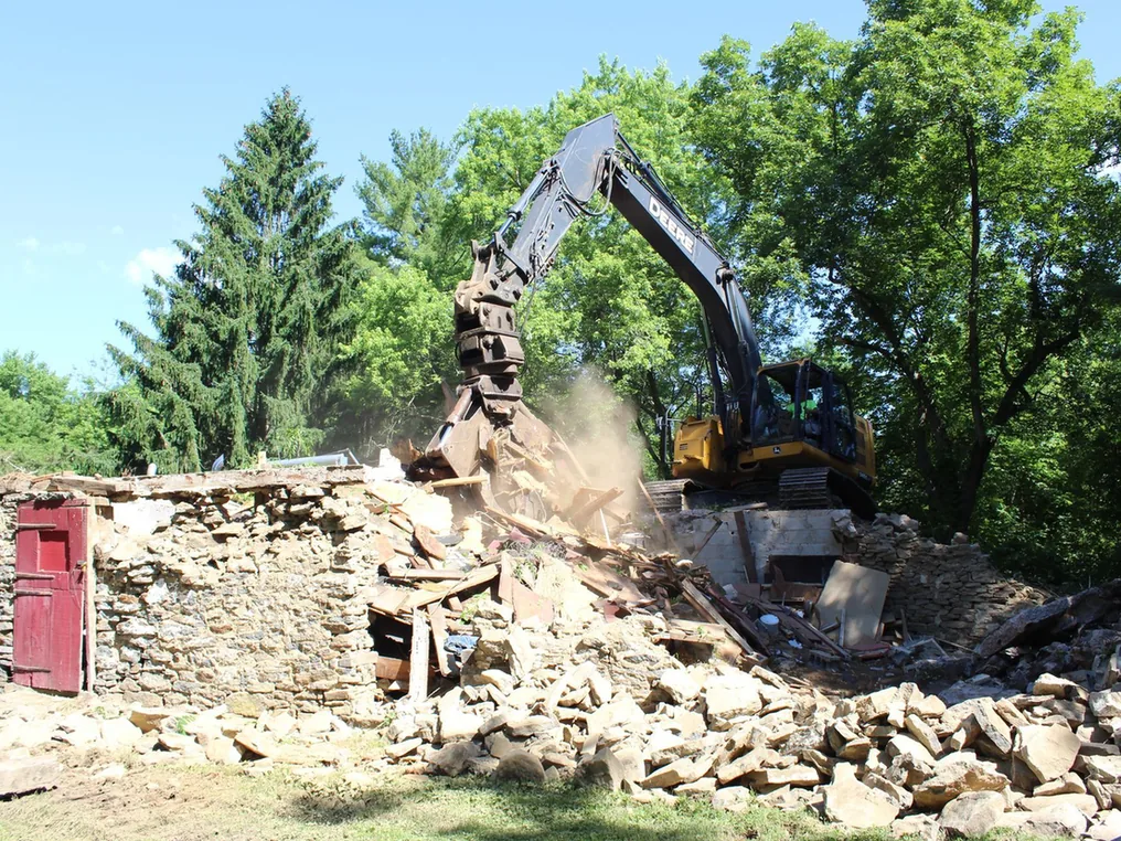 Excavator with a grapple bringing old fieldstone walls down into a rubble pile, house demolition