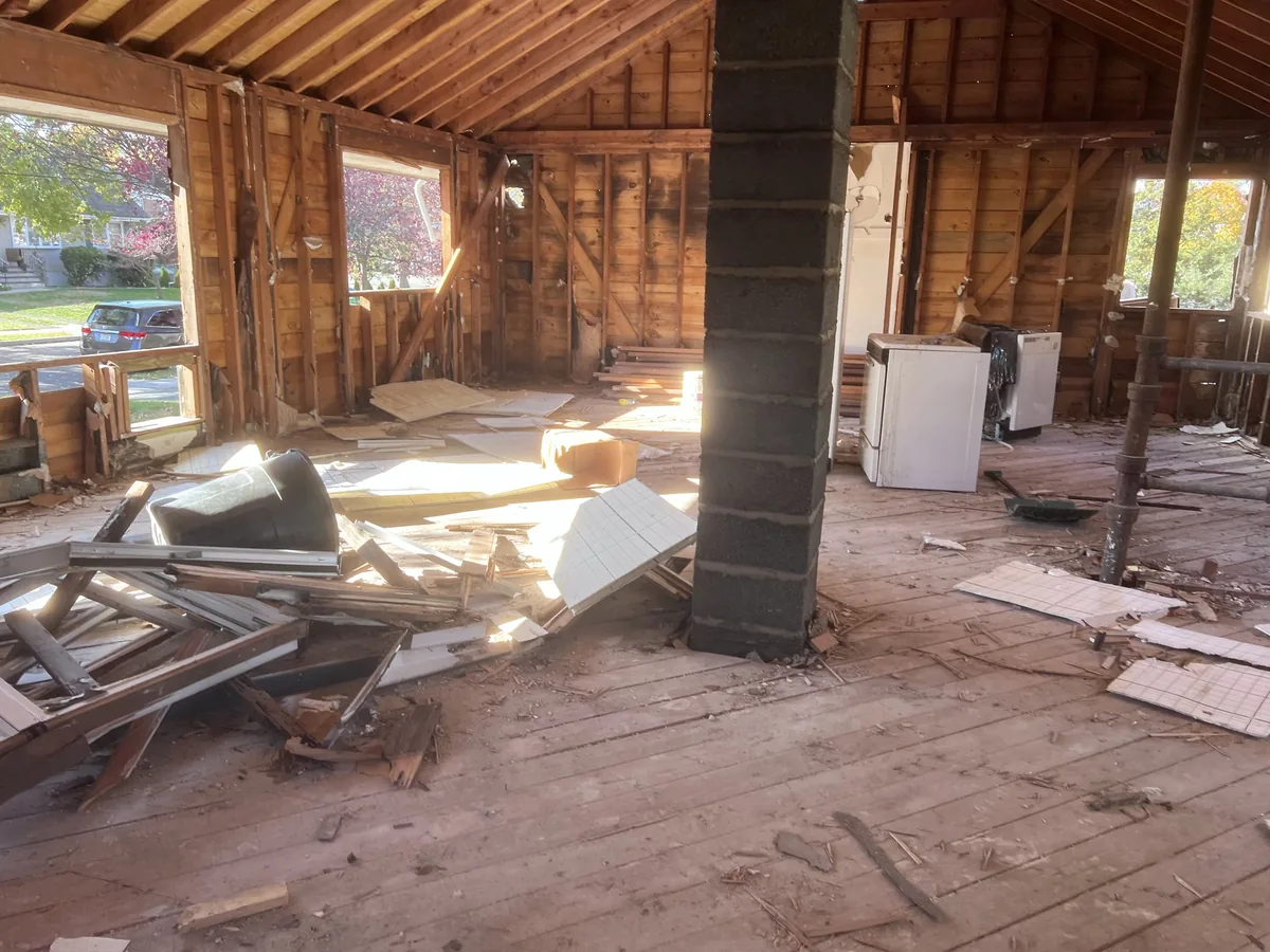 House interior gutted to the wall studs and roof rafters with debris on the floor, interior demolition