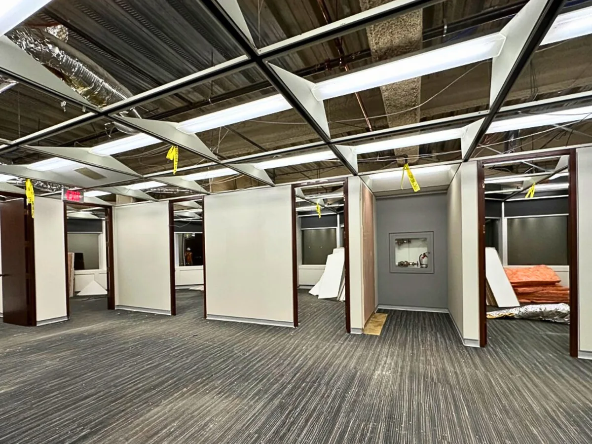 Office floor with the ceiling tiles removed and the ceiling grid, lights and ductwork exposed, interior demolition
