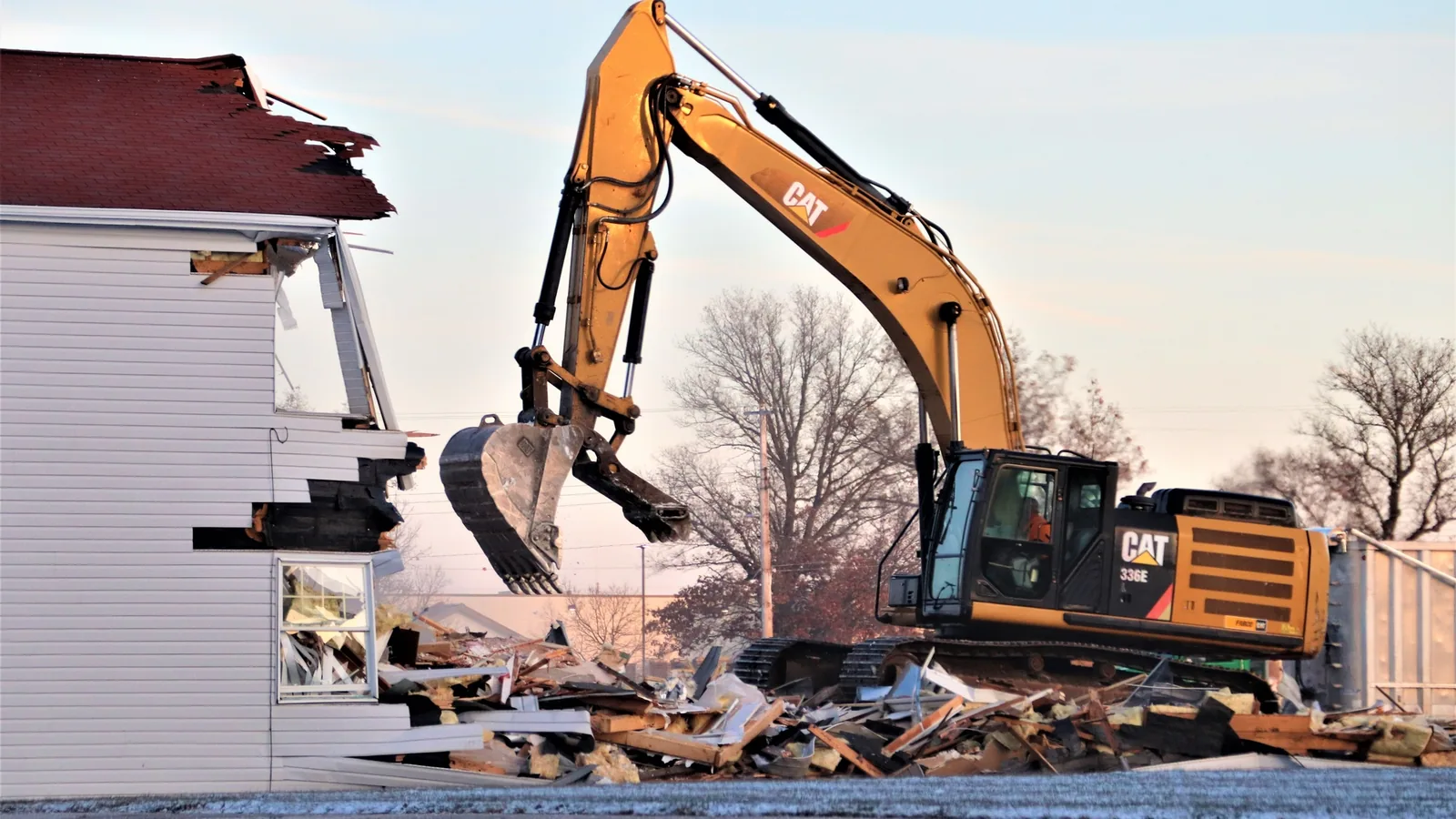 Excavator tearing apart a two story building beside a debris pile, demolition and masonry contractor